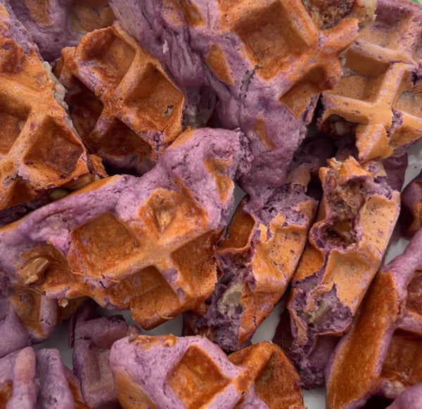 Close-up of broken Ube BAE Banana Foster Protein Waffle pieces showing purple and golden-brown colors and texture.